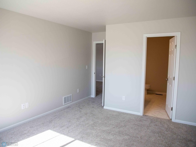 unfurnished bedroom featuring light carpet and ensuite bath