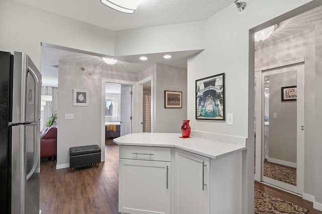 kitchen with dark hardwood / wood-style flooring, white cabinetry, light stone countertops, a textured ceiling, and stainless steel refrigerator