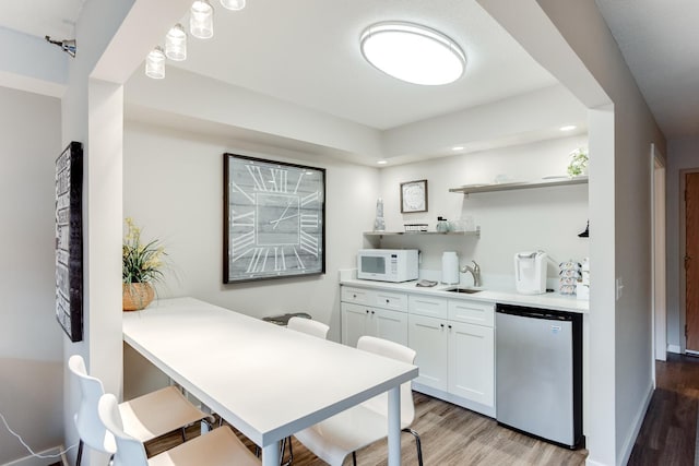 kitchen with light hardwood / wood-style flooring, sink, a breakfast bar, stainless steel dishwasher, and white cabinetry