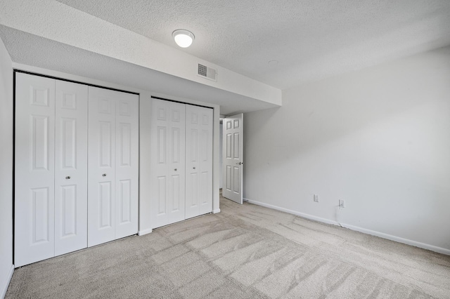 unfurnished bedroom with light colored carpet, a textured ceiling, and two closets