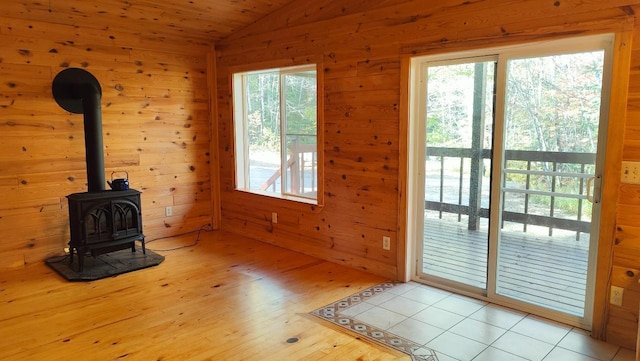 unfurnished living room with a wood stove, wood walls, lofted ceiling, and light wood-type flooring