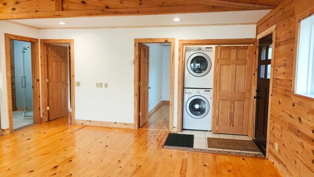 laundry room featuring wooden walls, stacked washer / drying machine, light wood finished floors, recessed lighting, and baseboards