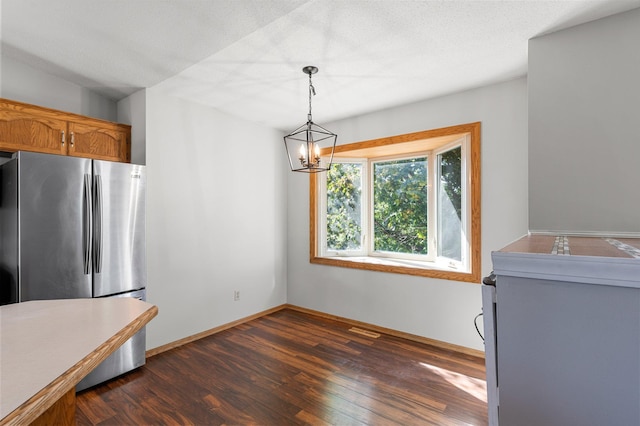 kitchen with dark wood-type flooring, stainless steel refrigerator, hanging light fixtures, an inviting chandelier, and a textured ceiling