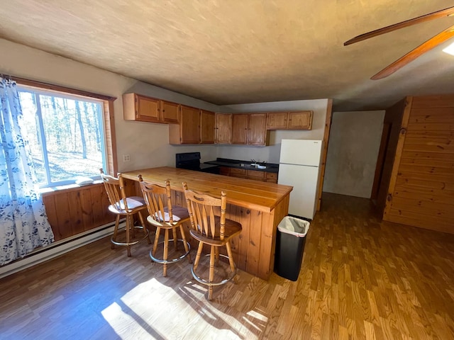 kitchen featuring light wood-type flooring, a breakfast bar area, black range oven, kitchen peninsula, and white fridge