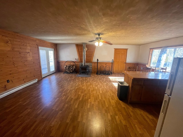 interior space with wood walls, ceiling fan, wood-type flooring, a wood stove, and french doors