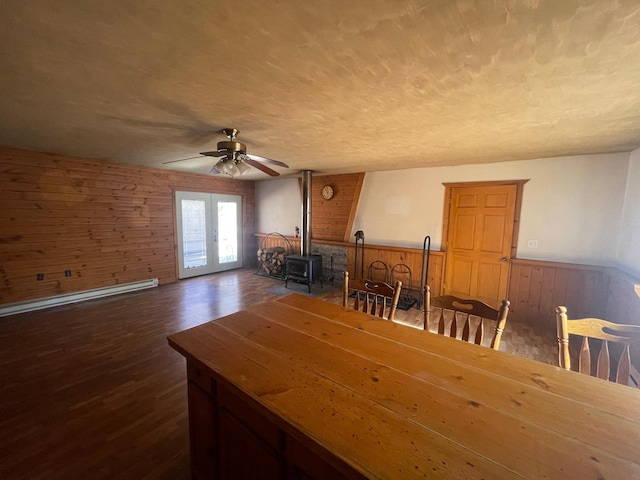 unfurnished dining area featuring dark wood-type flooring, wood walls, french doors, and a wood stove