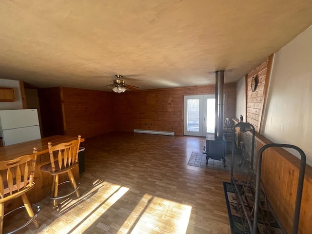 dining area featuring a wood stove, ceiling fan, a baseboard radiator, and wood-type flooring