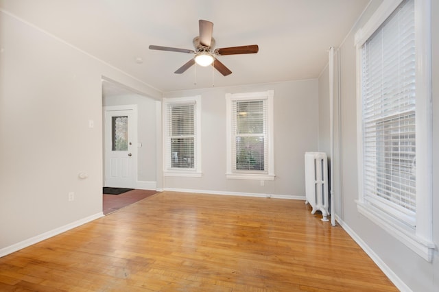 empty room featuring radiator heating unit, light hardwood / wood-style floors, and ceiling fan