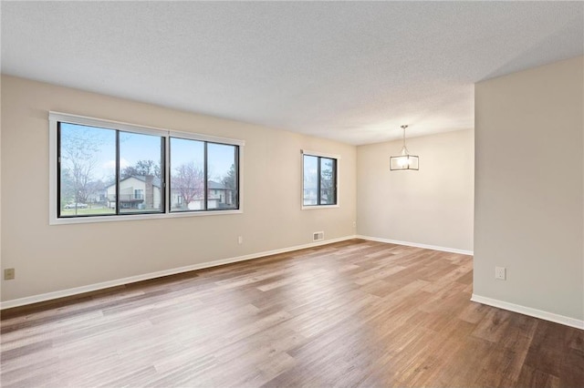 empty room with hardwood / wood-style floors, a notable chandelier, and a textured ceiling