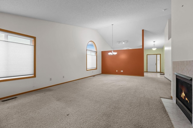 unfurnished living room with a tile fireplace, an inviting chandelier, high vaulted ceiling, a textured ceiling, and light carpet