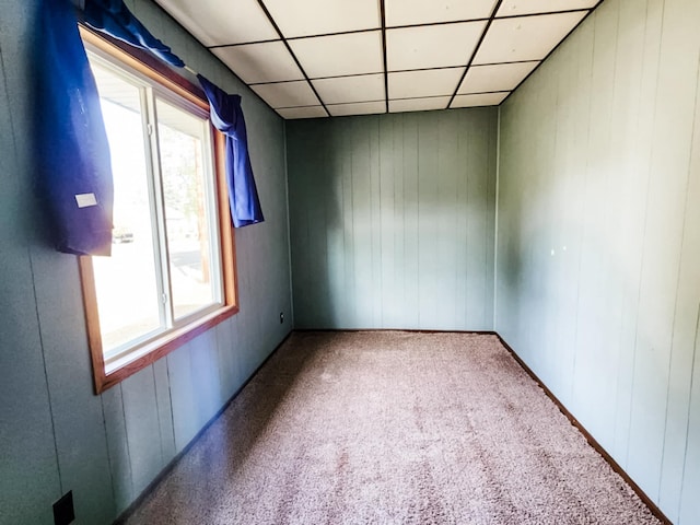 carpeted empty room with a drop ceiling and wooden walls