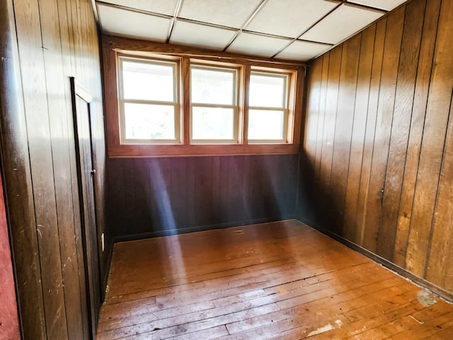 unfurnished room with wood-type flooring, a drop ceiling, and wood walls