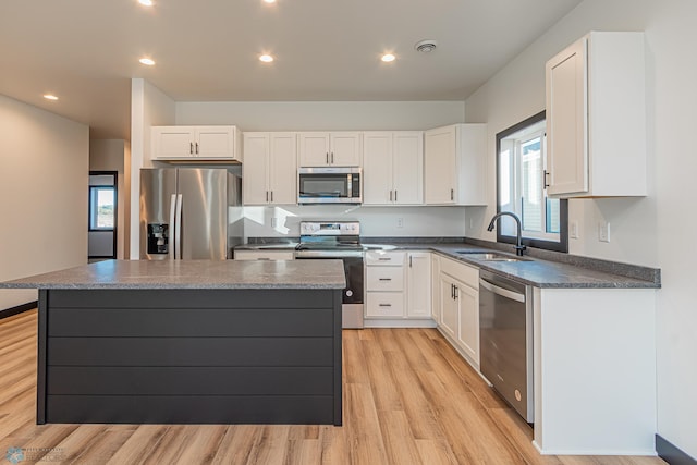 kitchen with appliances with stainless steel finishes, sink, white cabinetry, and a kitchen island