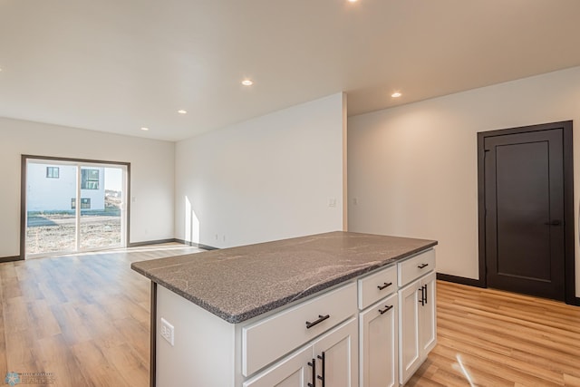 kitchen with dark stone counters, light wood-type flooring, a center island, and white cabinetry