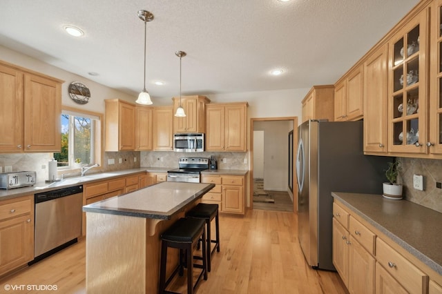 kitchen featuring a center island, appliances with stainless steel finishes, decorative light fixtures, light hardwood / wood-style floors, and a breakfast bar area