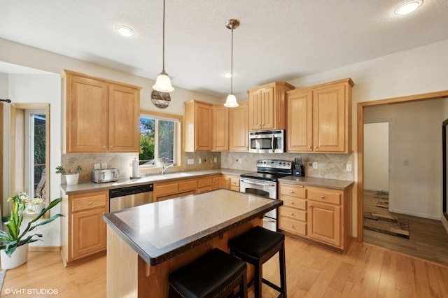 kitchen featuring a center island, light brown cabinets, a kitchen breakfast bar, light hardwood / wood-style floors, and appliances with stainless steel finishes