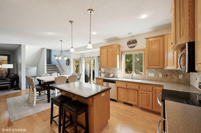 kitchen with stainless steel appliances, a kitchen island, hanging light fixtures, and light hardwood / wood-style floors