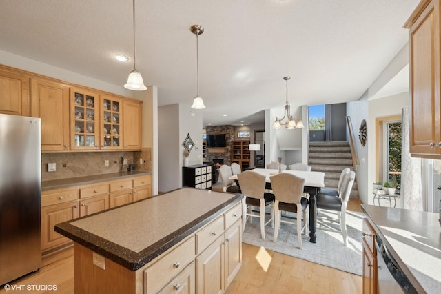 kitchen with a center island, backsplash, decorative light fixtures, appliances with stainless steel finishes, and light wood-type flooring