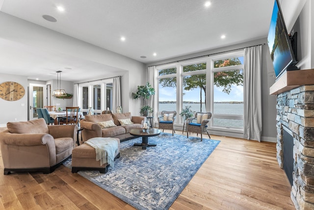 living room with a stone fireplace, light hardwood / wood-style floors, and a water view