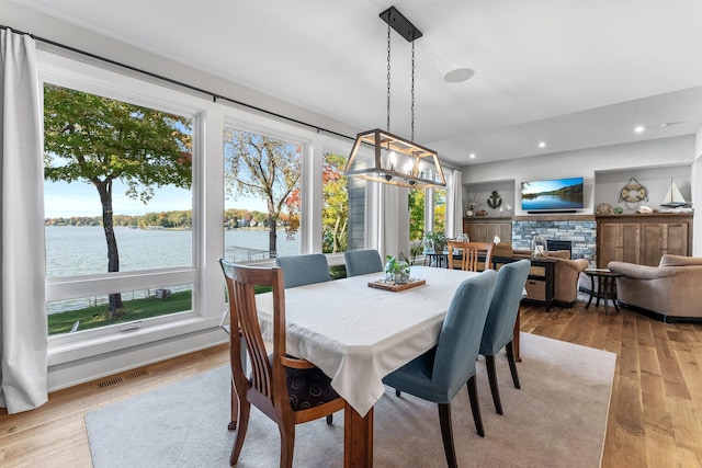 dining space with a water view, a fireplace, and light hardwood / wood-style floors