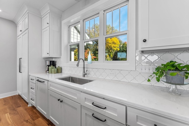 kitchen with hardwood / wood-style floors, sink, light stone countertops, backsplash, and white cabinets