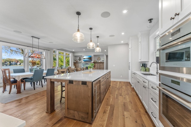 kitchen featuring light hardwood / wood-style flooring, decorative light fixtures, sink, a center island, and white cabinetry