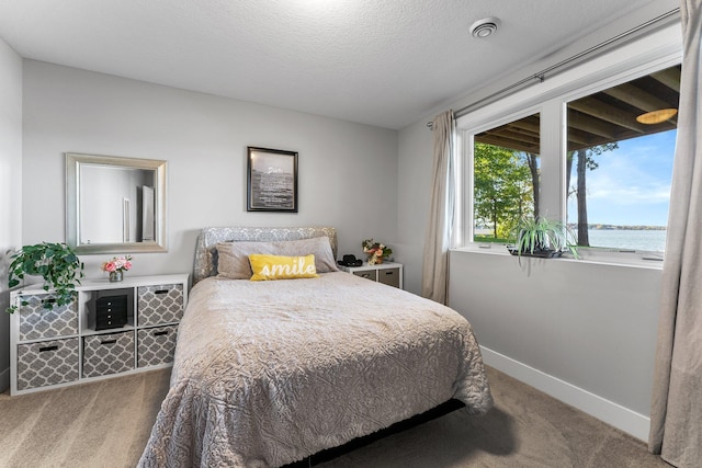 bedroom with a water view, carpet flooring, and a textured ceiling