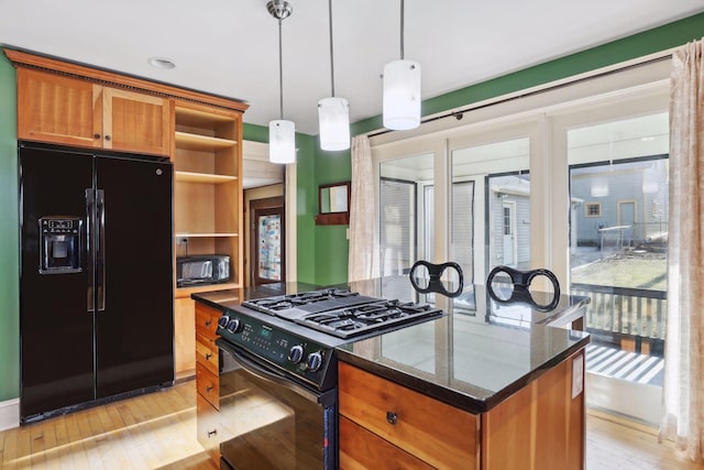 kitchen with hanging light fixtures, light hardwood / wood-style flooring, dark stone countertops, a kitchen island, and black appliances