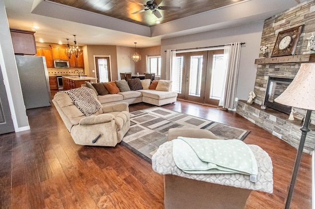 living room with sink, dark hardwood / wood-style flooring, a tray ceiling, a fireplace, and ceiling fan with notable chandelier