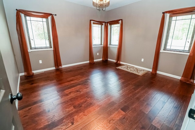 spare room with dark hardwood / wood-style floors, a wealth of natural light, and a notable chandelier