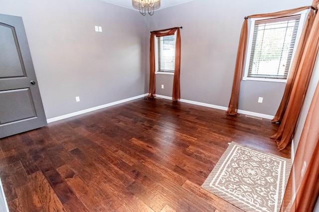 empty room featuring plenty of natural light, dark hardwood / wood-style floors, and a notable chandelier