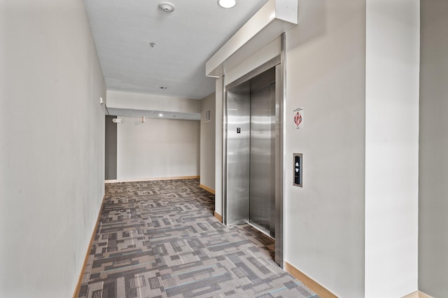 hallway with dark carpet and elevator