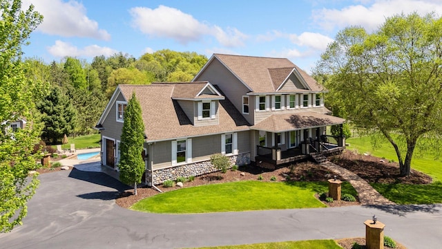 view of front facade with an attached garage, covered porch, asphalt driveway, and a front lawn