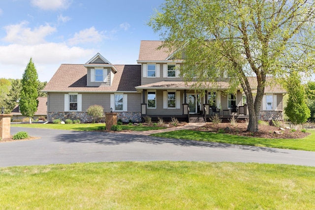 craftsman house with covered porch, a front lawn, stone siding, and a shingled roof
