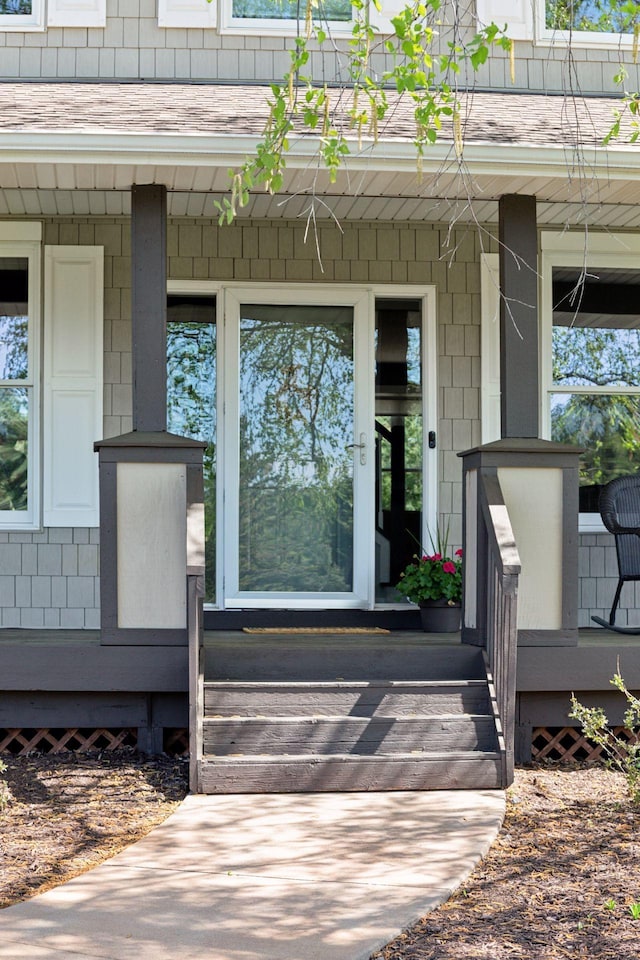view of exterior entry featuring covered porch and a shingled roof