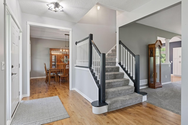 foyer entrance with stairs, ornate columns, wood finished floors, a chandelier, and a textured ceiling