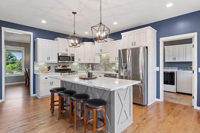 kitchen featuring appliances with stainless steel finishes, washing machine and dryer, a sink, a chandelier, and white cabinetry