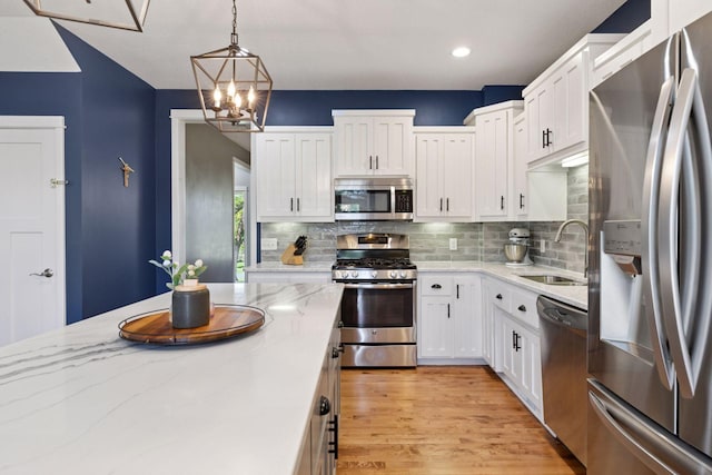 kitchen featuring stainless steel appliances, a sink, white cabinets, decorative light fixtures, and tasteful backsplash