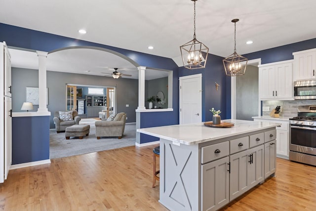 kitchen featuring appliances with stainless steel finishes, ornate columns, ceiling fan, a center island, and arched walkways