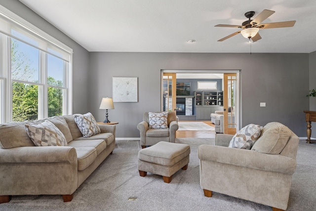 carpeted living area with baseboards and ceiling fan