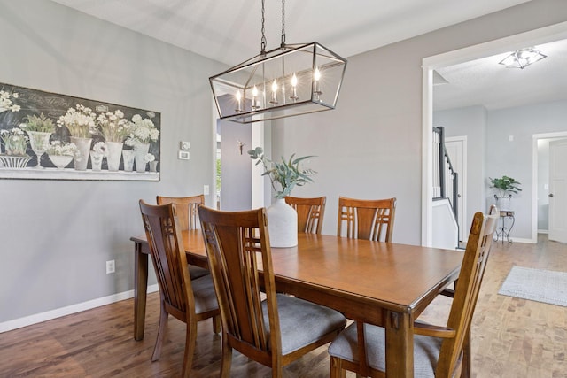 dining space with a chandelier, wood finished floors, baseboards, and stairs