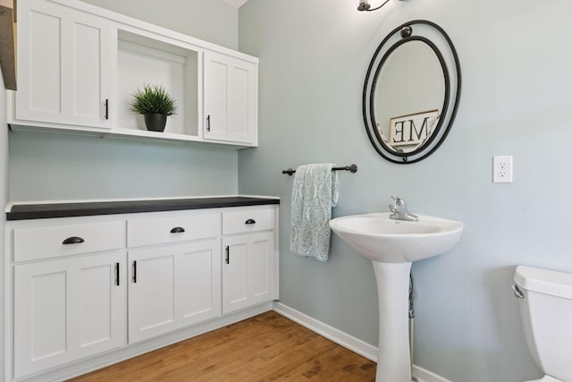 half bathroom featuring baseboards, toilet, and wood finished floors
