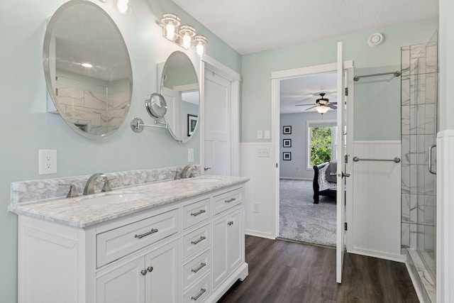 full bathroom featuring wood finished floors, a shower stall, double vanity, ceiling fan, and a textured ceiling