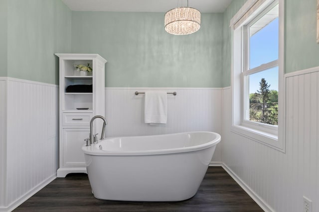 full bath with wood finished floors, a wainscoted wall, a soaking tub, and a chandelier