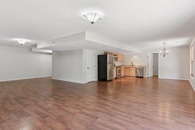 unfurnished living room featuring a chandelier, baseboards, a sink, and dark wood-style flooring