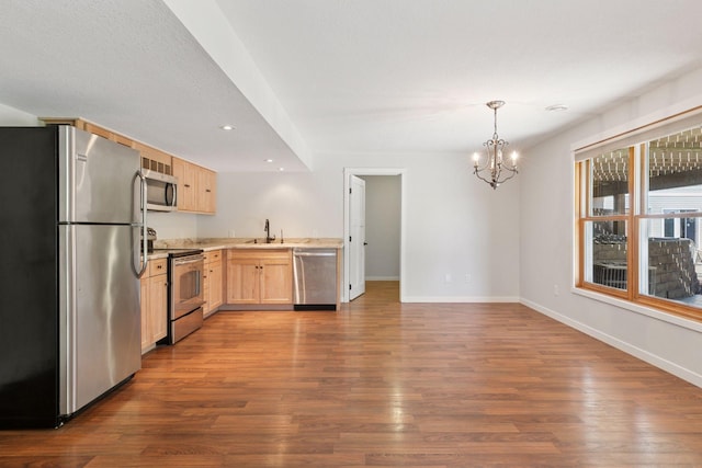 kitchen with stainless steel appliances, light brown cabinetry, a sink, a chandelier, and baseboards