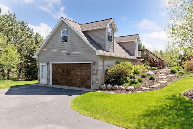view of side of property featuring an attached garage, roof with shingles, driveway, a yard, and stone siding