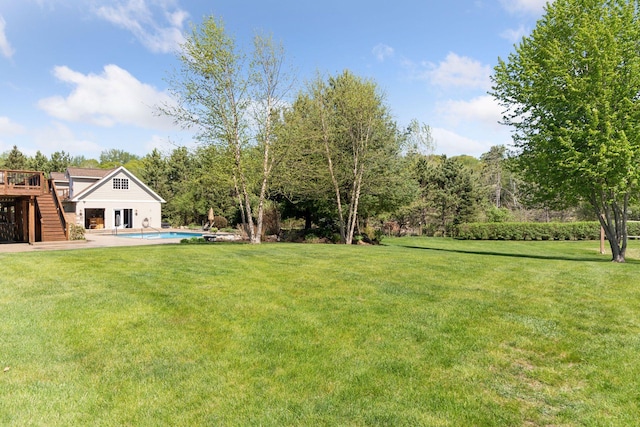 view of grassy yard with stairway, a wooden deck, and an outdoor pool