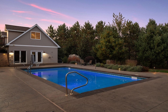pool at dusk with french doors, a patio area, and an outdoor pool
