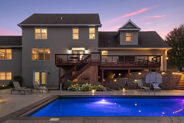 back of property at dusk featuring stairway, a wooden deck, a patio area, and an outdoor pool